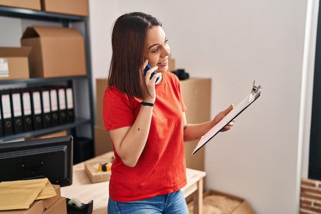 Free photo young beautiful hispanic woman ecommerce business worker talking on smartphone reading document at office