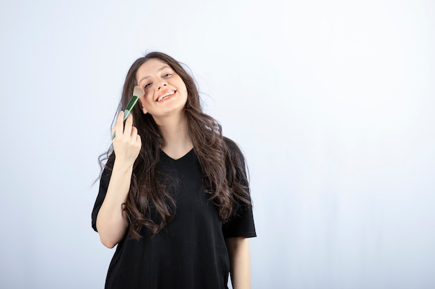 young beautiful model applying shadow with brush on white wall. 