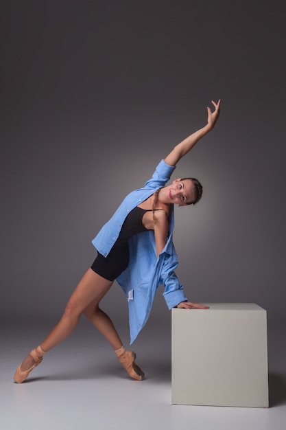  young beautiful modern style dancer posing on white cube on a studio gray background