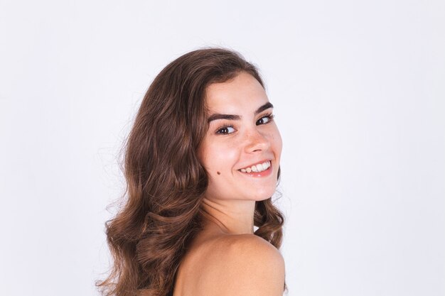 Young beautiful natural soft clean skin woman with freckles light makeup on white wall with bare shoulders