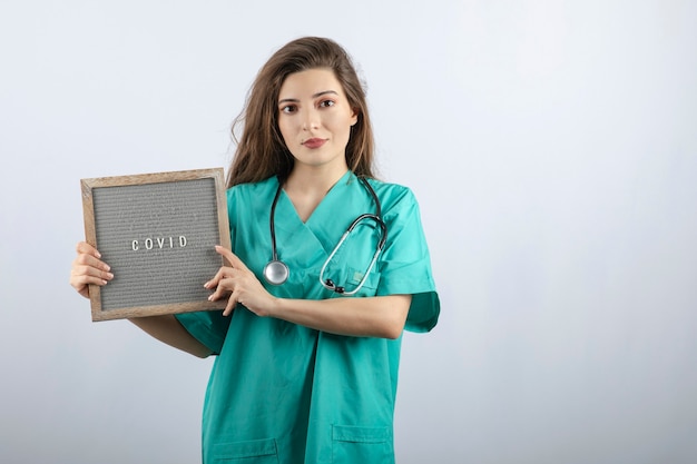 Young beautiful nurse in green uniform with stethoscope holding a frame 