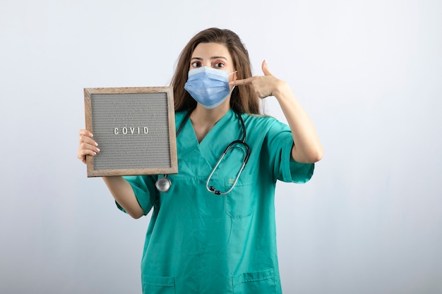 Young beautiful nurse in medical mask with a frame pointing at medical mask