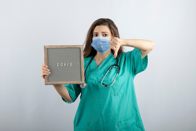 Young beautiful nurse in medical mask with a frame showing a thumb down