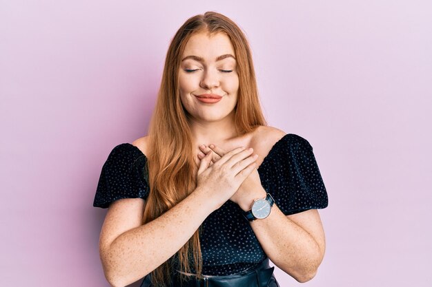 Young beautiful redhead woman wearing elegant and sexy look smiling with hands on chest, eyes closed with grateful gesture on face. health concept.