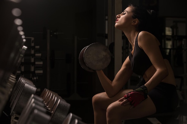 Young beautiful sexy blonde athlete bodybuilder exercises in the gym in beautiful sportswear on a dark background