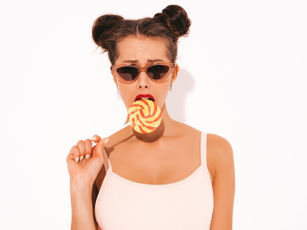 Free photo young beautiful sexy hipster woman with red lips in sunglasses.trendy girl in summer swimwear clothes. eating,biting candy lollipop