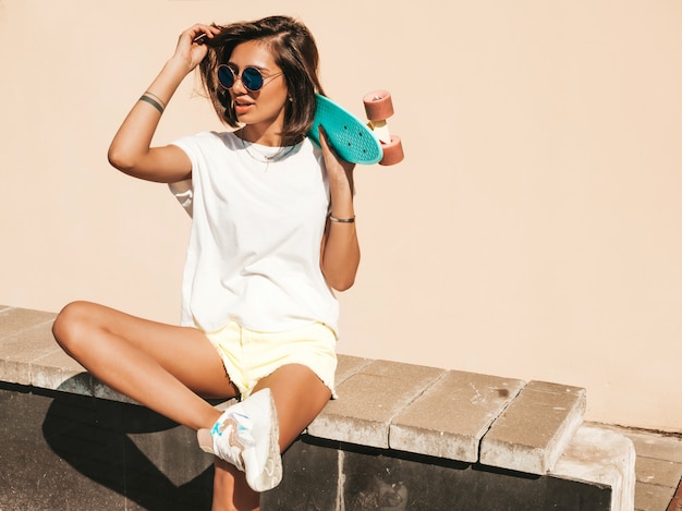 Free photo young beautiful sexy smiling hipster woman in sunglasses.trendy girl in summer t-shirt and shorts.positive female with blue penny skateboard posing on the street background