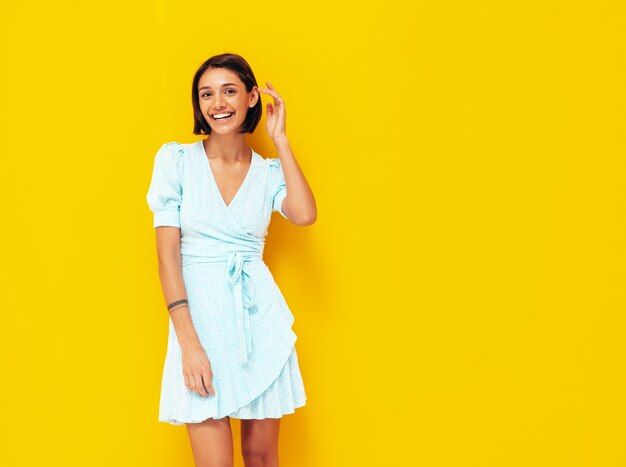 Young beautiful smiling female in trendy summer blue dress Sexy carefree woman posing near yellow wall in studio Positive model having fun Cheerful and happy Isolated