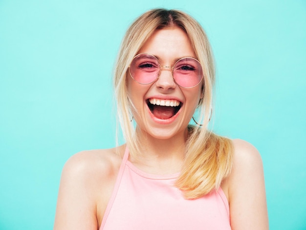 Young beautiful smiling female in trendy summer clothes Sexy carefree woman posing near blue wall in studio Positive model having fun Cheerful and happy In sunglasses Screaming and shouting