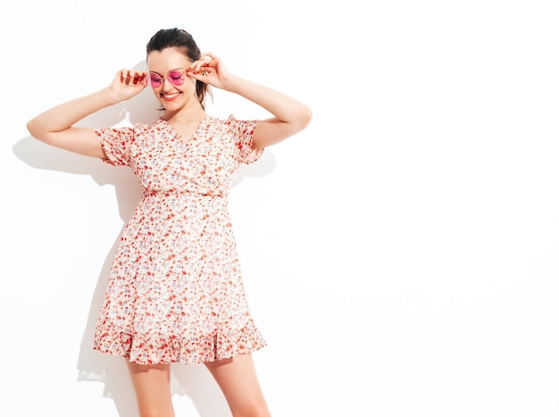 Young beautiful smiling female in trendy summer dress Sexy carefree woman posing near red wall in studio Positive brunette model having fun and going crazy Cheerful and happy