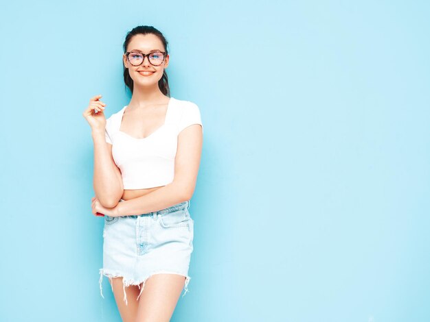 Young beautiful smiling female in trendy summer jeans skirt and top clothes Sexy carefree woman posing near blue wall in studio Positive brunette model having funCheerful and happy