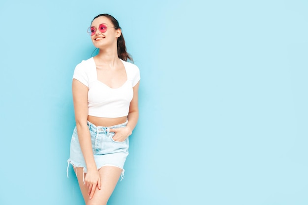 Free photo young beautiful smiling female in trendy summer jeans skirt and top clothes sexy carefree woman posing near blue wall in studio positive brunette model having funcheerful and happy