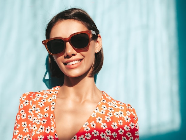 Young beautiful smiling female in trendy summer red dress Sexy carefree woman posing near blue wall in studio Positive model having fun Cheerful and happy At sunny day Shadow from window