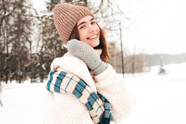 Free Photo young beautiful smiling hipster female in trendy warm clothes and scarf.carefree woman posing in the street in park. positive pure model having fun in snow. enjoying winter moments