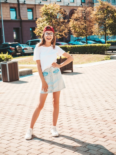 Free photo young beautiful smiling hipster woman in trendy summer clothes sexy carefree woman posing on the street background in cap at sunset positive model outdoors cheerful and happy in sunglasses