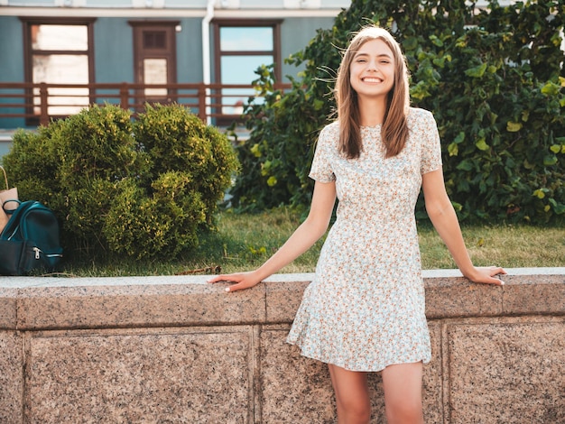 Free photo young beautiful smiling hipster woman in trendy summer dress sexy carefree woman posing on the street background at sunset positive model outdoors cheerful and happy with handbag