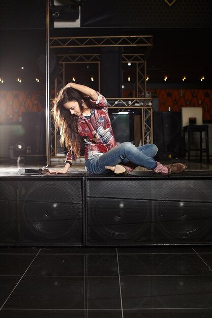 young beautiful smiling pop star singer with microphone sitting on the scene in the club