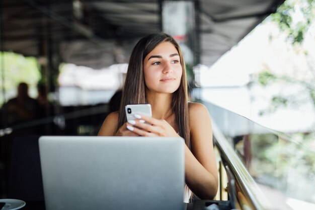 Young beautiful student girl with laptop and cup of tea or coffee in cafe