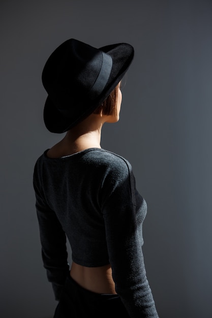 Young beautiful woman in black hat standing back to camera