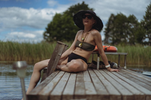 young beautiful woman in a black straw hat relaxes in the summer outdoors by the lake, by the water