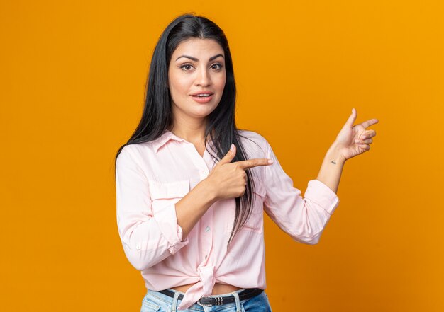 Young beautiful woman in casual clothes looking smiling confident happy and positive pointing with index finger to the side