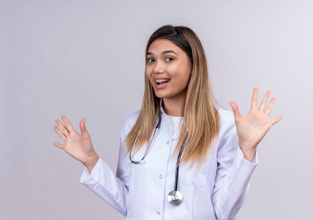 Young beautiful woman doctor wearing white coat with stethoscope looking uncertain and confused spreading palms having doubts