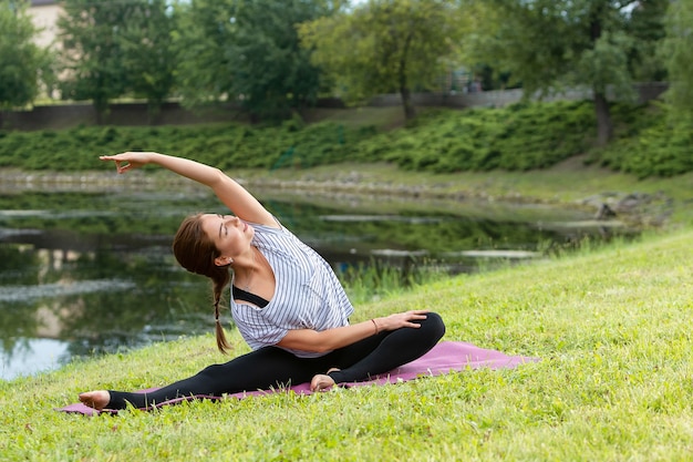 Young beautiful woman doing yoga exercise in green park. Healthy lifestyle and fitness concept.