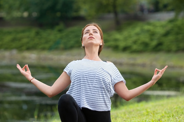 Young beautiful woman doing yoga exercise in green park