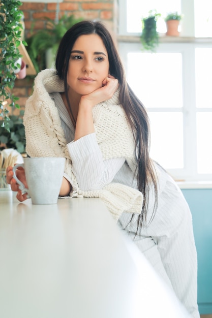 Young beautiful woman drinking a hot drink in the kitchen