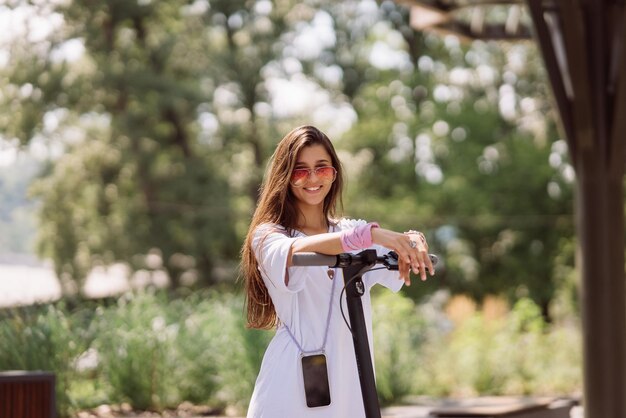 Young beautiful woman and electric scooter in the park