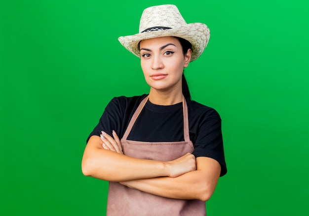 Young beautiful woman gardener in apron and hat with serious face with crossed hands 