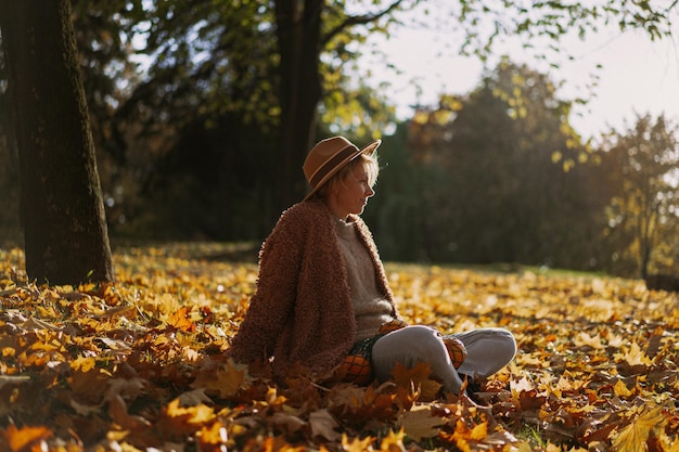 Young beautiful woman in a hat in an autumn park, a string bag with oranges, a woman throws up autumn leaves. Autumn mood, bright colors of nature.