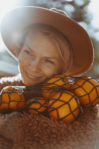 Free photo young beautiful woman in a hat in an autumn park, a string bag with oranges, a woman throws up autumn leaves. autumn mood, bright colors of nature.