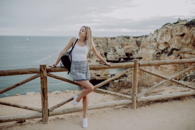 Young beautiful woman hipster traveler looking at sunset and beautiful seascape with a lookout point.