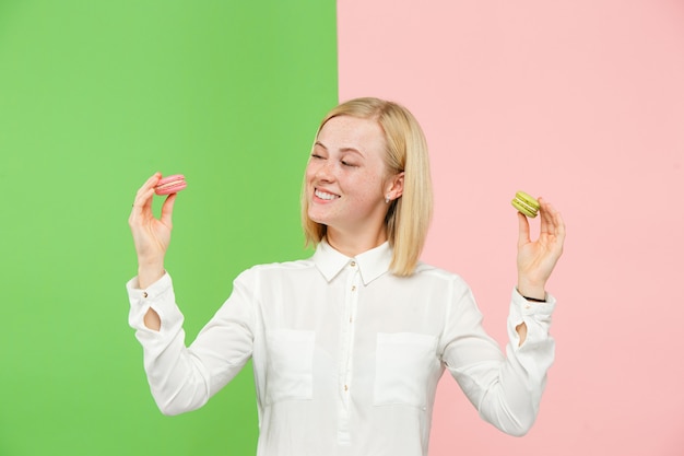 Free Photo young beautiful woman holding macaroons pastry in her hands, over trendy colored background at studio.