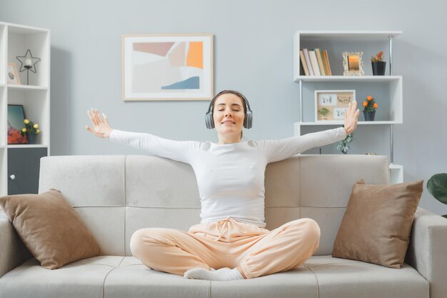 Young beautiful woman in home clothes sitting on a couch at home interior with headphones happy and positive relaxing spending weekend at home