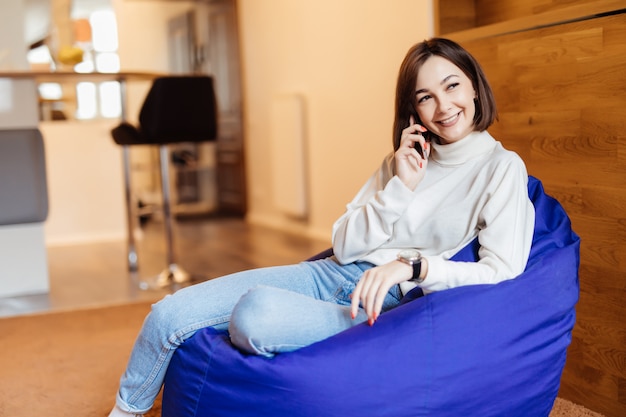 Free Photo young beautiful woman is sitting in bright violet bag chair using her phone texting