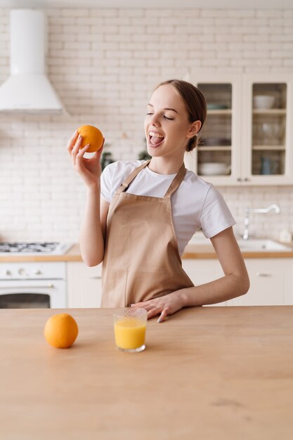 Young beautiful woman in the kitchen in an apron, fruits and orange juice