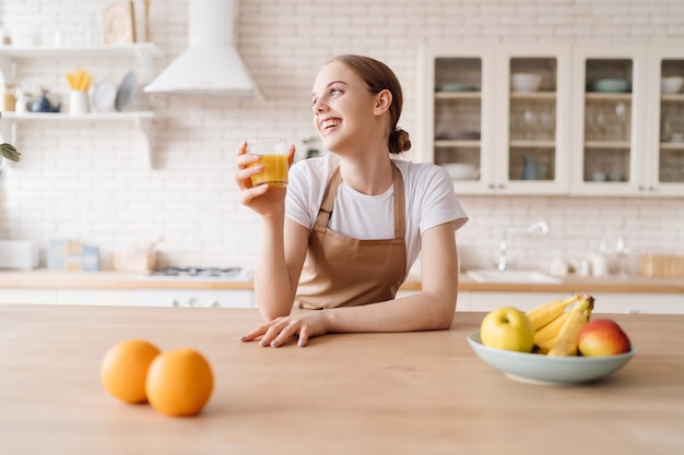 Free photo young beautiful woman in the kitchen in an apron, fruits and orange juice