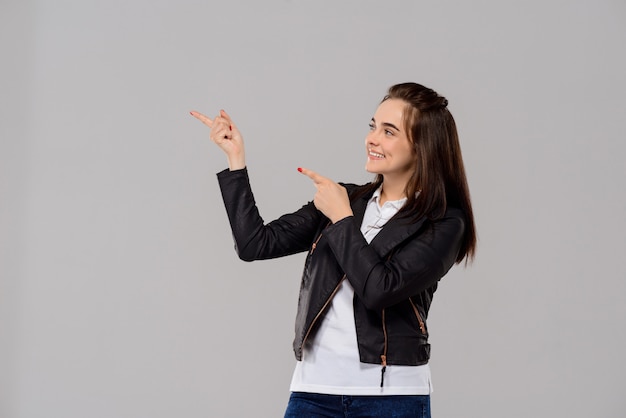 Young beautiful woman pointing fingers in side over purple wall