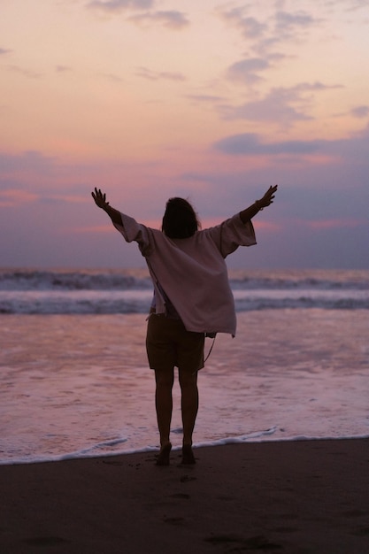 Free photo a young beautiful woman on the shore of the ocean at sunset enjoys freedom, place, time. view from the back. flowing clothes.