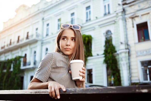 Young beautiful woman sitting on bench, holding coffee