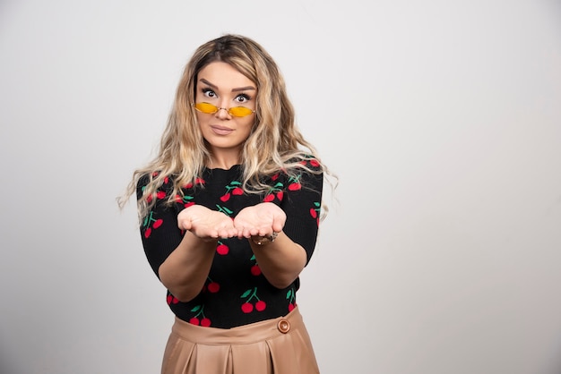 Free photo young beautiful woman standing over gray wall with hands palms together receiving or giving gesture.