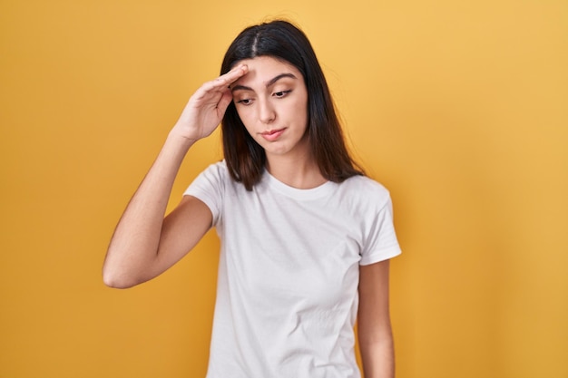 Young beautiful woman standing over yellow background worried and stressed about a problem with hand on forehead nervous and anxious for crisis