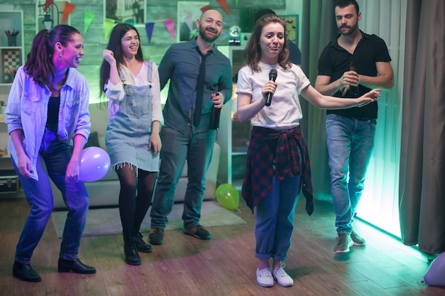 Free Photo young beautiful woman surrounded by her friends doing karaoke at the party.