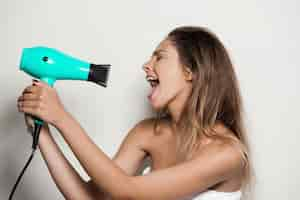 Free photo young beautiful woman in towel singing with hairdryer