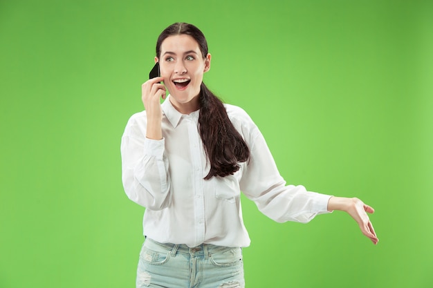 Young beautiful woman using mobile phone studio on green color studio background. Human facial emotions concept. Trendy colors