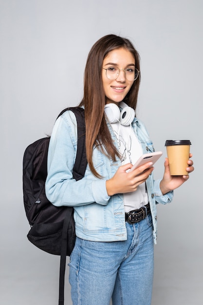 Young beautiful woman using smart phone with coffee isolated on white wall