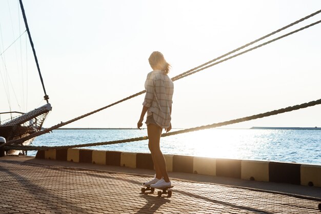 Young beautiful woman walking at seaside, skateboarding