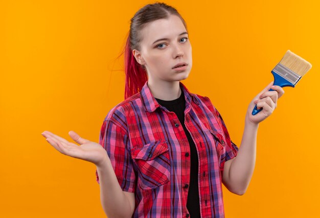  young beautiful woman wearing red shirt holding paint brush on isolated yellow wall